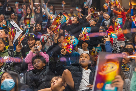 Excited students sit in Honda Center holding up workbooks